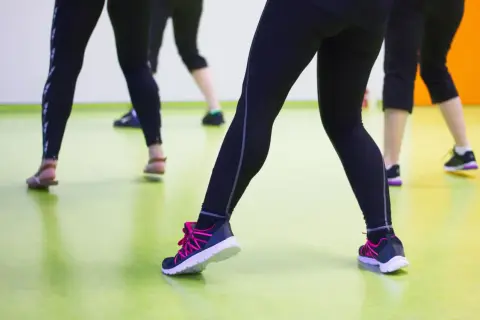 Ludzie w legginsach i butach sportowych ćwiczą na sali. Może właśnie dlatego buty skrzypią?