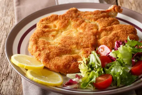 Chrupiący kotlet milanese z cytryną i świeżą sałatką z pomidorkami.