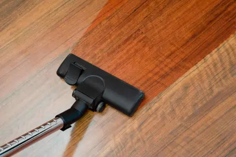 Cabezal de aspiradora limpiando suelo laminado. El suelo laminado se ve brillante y limpio tras pasar la aspiradora.