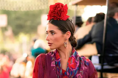 Mujer con flor flamenca en su pelo corto, pendientes llamativos y mantón bordado.