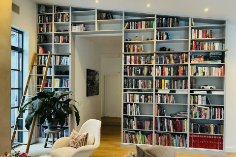 En stor inbyggd bokhylla med en stege, fylld med böcker och prydnadssaker. Perfekt inbyggd bokhylla inspiration för ett bibliotek.