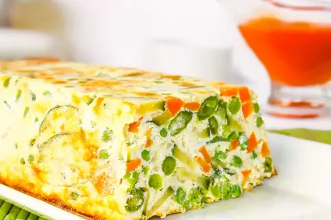 Un delicioso pastel de verduras, con guisantes, zanahoria y calabacín, horneado en un molde rectangular.