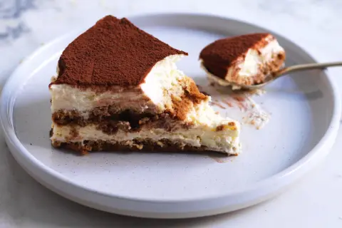 Una fetta di tiramisù, con cacao in polvere, su un piatto. La ricetta perfetta per un dolce cremoso e goloso.