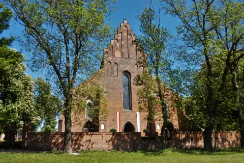 Gotycka ceglana świątynia, prawdopodobnie kościół pw. św. Jadwigi, otoczona zielenią. W tle błękitne niebo. Halszka Szamotuły.