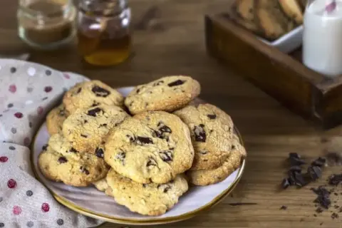 Montón de galletas con pepitas de chocolate recién horneadas, listas para disfrutar con un vaso de leche.