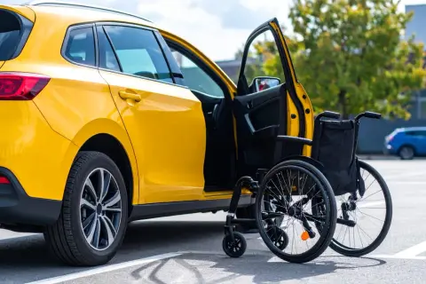 Auto gialla con portiera aperta e carrozzina. Informazioni su quanto costa passaggio di proprietà auto con legge 104.