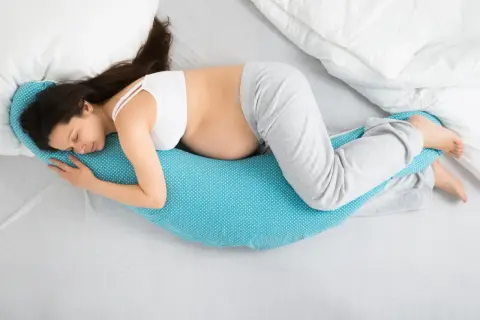 Mujer embarazada duerme de lado, abrazando una almohada de apoyo. Las posturas de dormir en el embarazo son clave para el descanso.