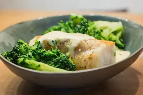 Un plat de queue de lotte poêlée, nappée d'une sauce crémeuse et accompagnée de brocolis croquants.