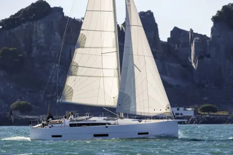 Un elegante catamarano solca acque azzurre, con vele bianche gonfie di vento, mentre sullo sfondo si stagliano scogliere rocciose.