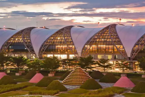 Der moderne Flughafen Bangkok Suvarnabhumi mit seiner markanten Dachkonstruktion und der kunstvollen Gartenanlage bei Sonnenuntergang.