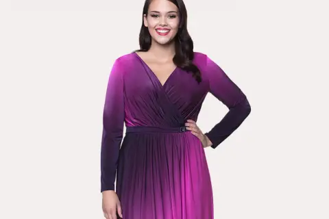 Uśmiechnięta modelka w butik na plus sukienki. Długa, fioletowo-różowa sukienka z dekoltem kopertowym i długimi rękawami.