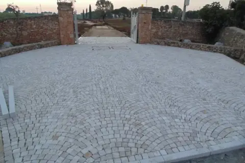 Un viale d'ingresso con un'elegante pavimentazione a ventaglio di sanpietrini texture, fiancheggiato da muretti in pietra e pilastri antichi.