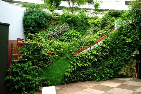 Una rigogliosa parete verde ricca di piante e fiori, con una scala rossa che attraversa la vegetazione.