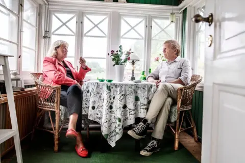 Britt Skogman och en man sitter vid ett bord i ett solrum.
