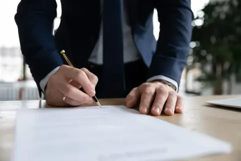 Mężczyzna w garniturze podpisuje dokument, który może być wypowiedzeniem umowy o pracę.