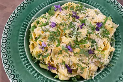 Krämig sparris pasta med färska örter och violblommor, toppad med riven parmesan. En härlig vårrätt!