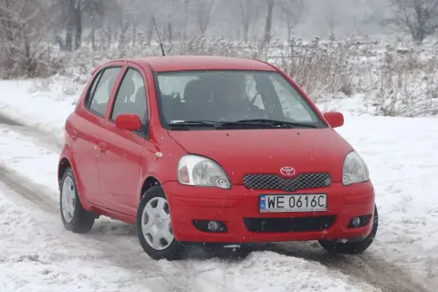 Czerwona Toyota Yaris 1 na śniegu. Kierowca przygotowuje się do wymiany żarówki.