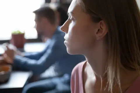 Kobieta z zamyśloną miną, być może zmagająca się z myślami typowymi dla osobowości anankastycznej, siedzi przy stole.