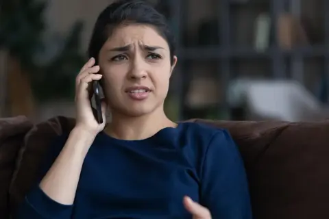 Zmartwiona kobieta rozmawia przez telefon, słysząc najgorsze opinie o loteriach "kredyt bez odsetek" dostępnych w internecie.