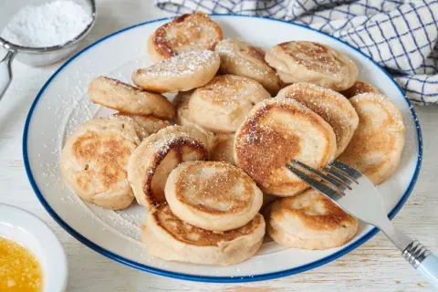 Ein Teller voller goldbrauner Poffertjes, bestäubt mit Puderzucker. Ein Gabel liegt bereit, um das leckere Poffertjes Rezept zu genießen.