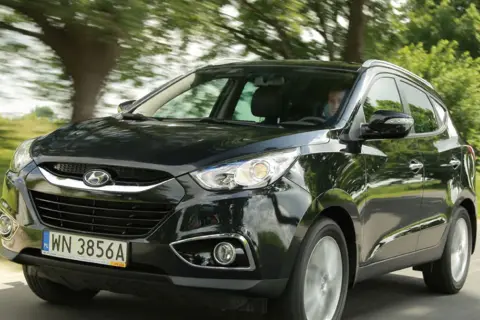 Czarny Hyundai ix35 2.0 benzyna w ruchu, z zielenią drzew w tle.