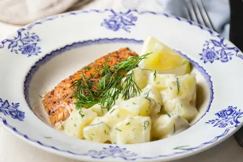 En bit lax med dill och en krämig stuvad potatis, serverad på en vacker blåvit tallrik.