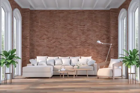Un salón moderno con una imponente pared de ladrillo visto, sofá blanco, sillón y plantas verdes.