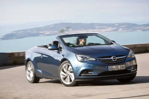 En blå Opel Cascada cabriolet kör längs en kustväg med havet i bakgrunden.