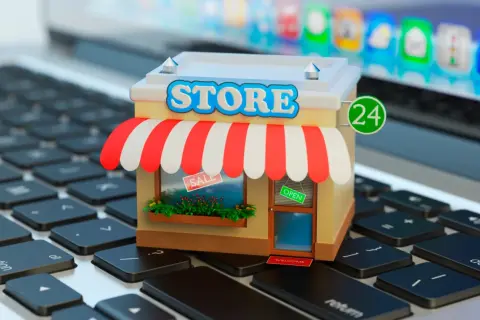 Miniatura de una tienda en línea sobre un teclado de portátil. La tienda tiene un letrero de "STORE", toldo a rayas y un cartel de "OPEN".