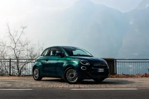 Zielony Fiat 500 na tle górskich krajobrazów. Wiele osób chwali ten model, a jego opinie są bardzo pozytywne.