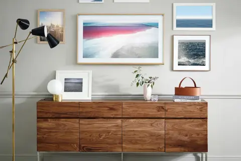 Ein moderner Wohnzimmerschrank aus Holz, der Kunstwerke und einen stilvollen Lampenständer präsentiert. Der große Bilderrahmen in der Mitte könnte einen **Fernseher verstecken**.