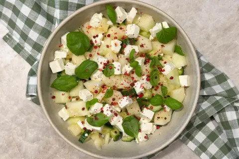 En uppfriskande melonsallad med honungsmelon, fetaost, gurka och basilika, toppad med rosa pepparkorn.