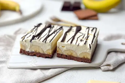 Zwei Stücke Bananensplit Torte mit Schokoladenboden, Bananenscheiben und cremiger Füllung, garniert mit Schokoladensauce.