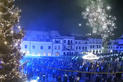 Świąteczna iluminacja i fajerwerki nad rynkiem w Kazimierzu Dolnym. Tłumy ludzi świętują nadchodzące wydarzenia.