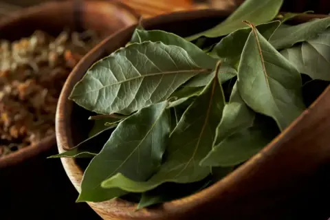 Hojas de laurel secas en un cuenco de madera, listas para dar sabor a guisos y estofados.