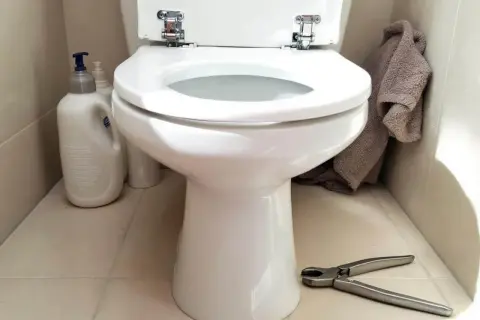 Préparation pour changer l'abattant WC : produits de nettoyage, serviette et pince à portée de main.