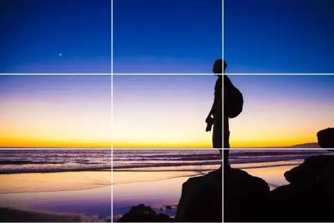 Sylwetka fotografa na tle zachodu słońca, z księżycem na niebie. Kompozycja zgodna z zasadami fotografii, z liniami siatki.