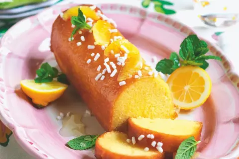 Torta facile glassata all'arancia, decorata con spicchi d'arancia, menta e zuccherini. Servita su un piatto rosa con spicchi di limone.
