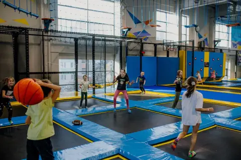 Dzieci skaczą na trampolinach, rzucają piłką i grają w gry. Wspaniałe zabawy na 30 urodziny w parku trampolin.