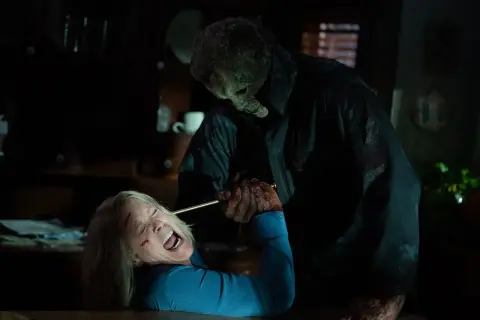 Michael Myers w masce i czarnym płaszczu trzyma nóż nad krzyczącą Laurie Strode. To przerażający halloweenowy finał.