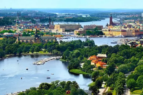 Widok na miasto z wodą i zielenią. W oddali widać budynki, a na pierwszym planie rzekę z łodziami. To piękny krajobraz, jakby z lotniska Nyo.