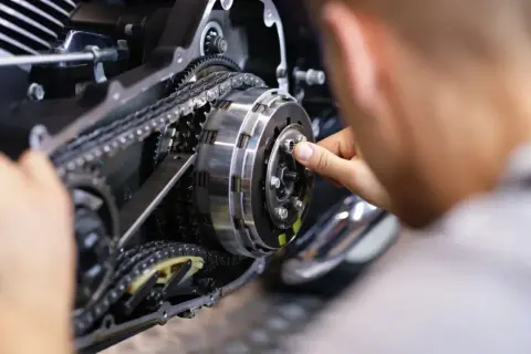 Mechanik naprawia sprzęgło motocykla, widoczny mechanizm z łańcuchem i zębatkami.
