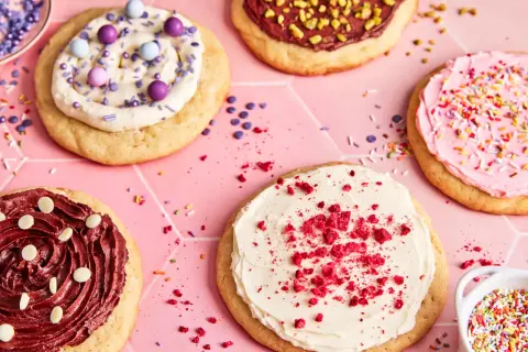 Bunte, verzierte Kekse, darunter ein mit weißer Creme und roten Krümeln bestreuter **crumble cookie**.
