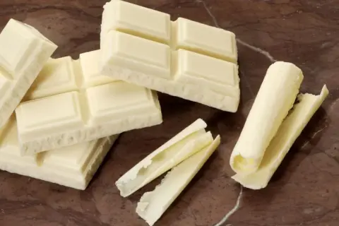 Barras de chocolate blanco, algunas enteras y otras desmenuzadas, demuestran que el chocolate blanco es chocolate.