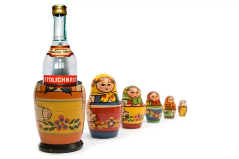 Butelka wódki Stolichnaya w drewnianej babuszce, otoczona mniejszymi matrioszkami.