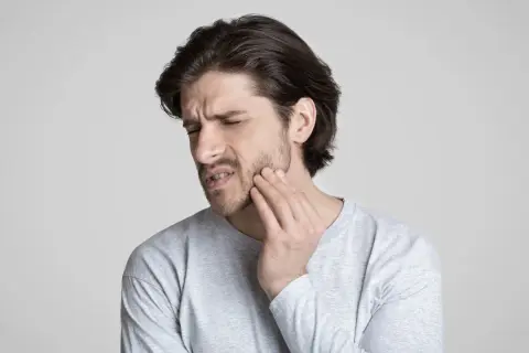 Uomo con mano sulla guancia, espressione di dolore. Potrebbe soffrire di disestesia o parestesia.