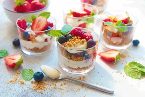 Délicieux **crumble fruits rouges** en verrines, garni de fraises, framboises, myrtilles et menthe. Une cuillère attend patiemment.