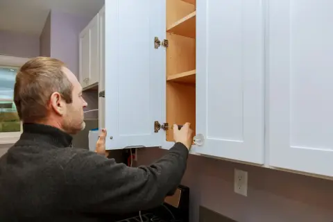 Hombre ajustando bisagras para como regular puertas de armario.