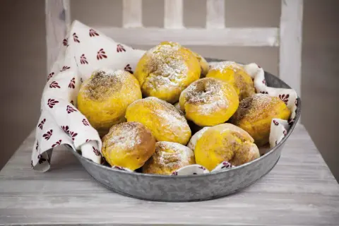En skål med gyllene julgodis med saffran, pudrade med florsocker, på en duk med mönster.