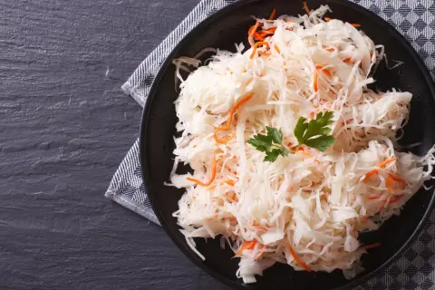 Ein Teller mit traditionellem Sauerkraut-Rezept, garniert mit Petersilie und Karottenstreifen, auf dunklem Stein serviert.